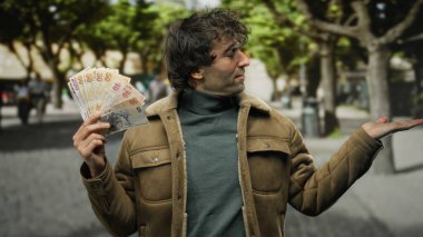 Bir şehir caddesinde elinde Türk lirası tutan İspanyol bir adam, canlı bir şehir ortamında açık bir el hareketi yapıyor..