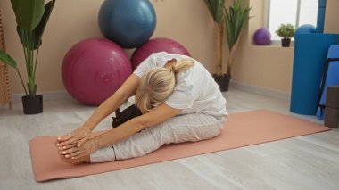 Egzersiz topları ve bitkilerle çevrili bir chihuahua köpeğiyle yoga minderinde uzanan orta yaşlı sarışın kadın..