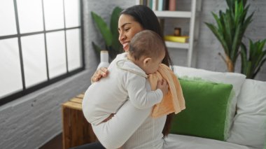 Yatak odasında bebeğini kucağında tutan kadın, aile sevgisini ve sıcaklığını penceresinden gelen doğal ışıkla gösteriyor..
