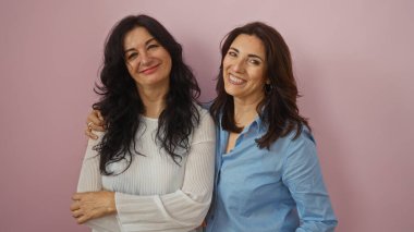 İki orta yaşlı kadın, muhtemelen kız kardeşler ya da arkadaşlar, soyutlanmış pembe bir arka plana karşı sıcacık gülümsüyorlar, sevgi, aile ve arkadaşlık simgesi..