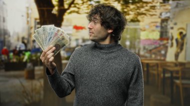 İspanyol adam, şehir merkezindeki bir kahve dükkanının yakınındaki bir sokakta elinde Czech Koruna banknotları tutuyor. Şehir hayatı ve finansal temalar sergiliyor..