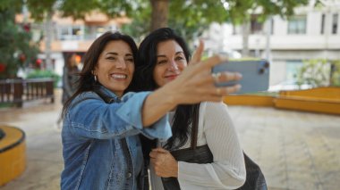 Hayat dolu bir parkta gülümseyen ve selfie çeken kadınlar şehrin arka planında neşeli anları yakalıyorlar. Dışarıdaki arkadaşlığı ve mutluluğu somutlaştırıyorlar..