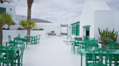 Ianzarote 'de, palmiye ağaçları ve kaktüs bitkileriyle beyazlatılmış arka planda yeşil sandalye ve masaların yer aldığı Meksika tarzı bir avlunun bulanık manzarası..