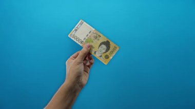 Güney Koreli bir adamın elinde mavi bir arkaplan, para bozdurma veya finansal konsept üzerinden banknot kazandı..
