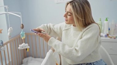 Beşikteki bebeğin fotoğrafını çeken kadın akıllı telefon kullanıyor, kapalı bir odada cep telefonu kullanıyor, genç ve güzel, özel anları yakalıyor, ebeveynlikteki teknolojiye odaklanıyor..