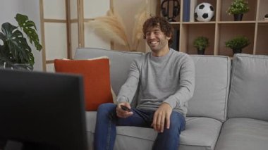 Oturma odasındaki uzaktan kumandalı koltukta oturan genç adam gülümseyerek boş zamanların tadını çıkarıyor.