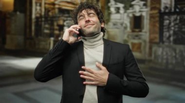 Şık giyinmiş genç bir adam şehir caddesinde telefonda neşeli bir şekilde konuşuyor..