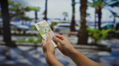 Kentsel açık hava ortamında Hong Kong dolarlarını tutan eller, şehrin hareketli ortamında mali işlem veya yatırıma işaret ediyor.