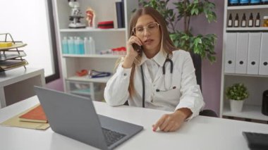 Doktor, klinikte bilgisayarlı ve tıbbi ekipmanlı telefonla konuşuyor. Profesyonel çevreyi gösteriyor..