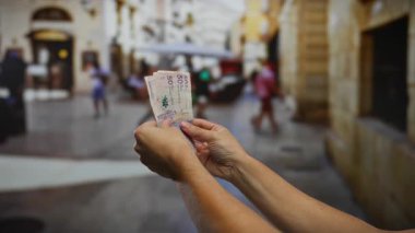 Kalabalık bir şehir caddesinde Kolombiya pezosu tutan adam, canlı bir açık şehir ortamında para değişimi sergiliyor..