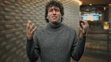 Hırkalı genç adam, kapalı alanda duvarlara karşı şaşkın bir ifadeyle.