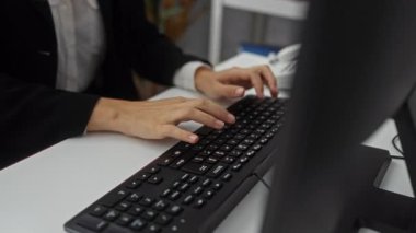 Modern ofiste klavyeyle yazı yazan bir kadın, sarışın ve odaklı, etrafı kitaplar ve yeşilliklerle çevrili, parlak bir iç mekanda, profesyonellik ve konsantrasyonu çağrıştırıyor..