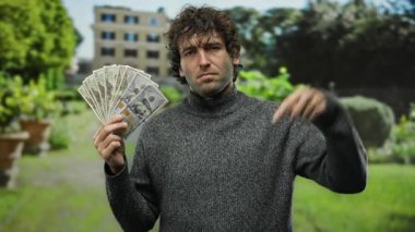 Parkta İspanyol bir adam Amerikan dolarlarını elinde tutarken aşağı doğru işaret ederek zenginliğin ve düşüncenin özünü yakalıyor..