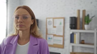 Ofis ortamında mor ceketli bir kadın modern dekorlu, kendinden emin, gözlüklü ve sarı saçlı.