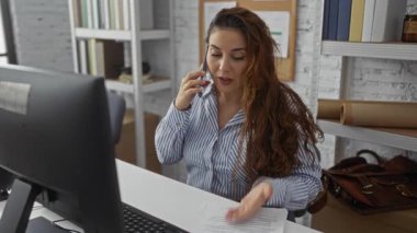 Modern ofis içinde masa başında konuşan bir kadın bilgisayar rafları ve rahat bir atmosferle konuşuyor.
