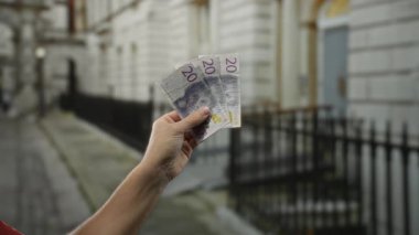 Bir şehir caddesinde elinde İsveç banknotları tutan adam, İsveç 'teki kentsel yaşamı ve finansal işlemleri vurguluyor..
