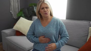 Rahat bir oturma odasında, modern bir evde mavi bir kazak giyerken rahatsız olan bir kadın..