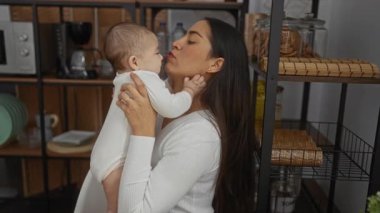 Kadın, sıcak mutfak ortamında bebeğini kucağında tutuyor sevgi ve sıcaklığı ifade ediyor aile anlarını evdeki eşyalarla ve sıcak aydınlatmayla sergiliyor..