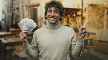 Elinde Polonya parası olan bir adam bir sokak kafesinde gülümsüyor ve Avrupa mimarisinin ipuçlarıyla canlı bir şehir atmosferi yaratıyor..