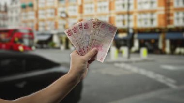 Kalabalık bir şehir caddesinde elinde Türk lirası banknotlar tutan, arka planda binalar ve arabalar olan bir adam, açık hava ortamında kentsel bir finans teması yakalıyor..