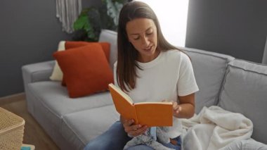 Kadın rahat bir oturma odasında uyuyan oğluna kitap okuyor aile sıcaklığını, sevgiyi ve huzurlu bir aile ortamını yakalıyor..