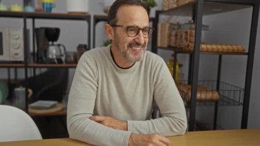 Ofis ortamında gülümseyen olgun bir adam. Arka planda raflar var. Kapalı bir ortamda güven ve mutluluk yayıyor..