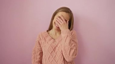 Yumuşak pembe arka plan karşısında neşeli bir şekilde gülen bir kadın rahat ve mutlu bir ruh hali içinde rahat bir kazak giyiyor.