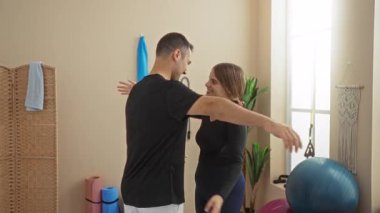 Spor salonunda spor aletleri ve doğal ışık temasını vurgulayan erkek ve kadın, kapalı bir spor merkezinde bir bağ olduğunu öne sürüyor..