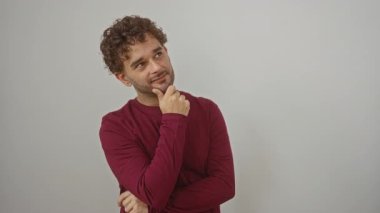 Genç İspanyol adam ayakta ve tişört giyiyor, düşünceli, düşünceli bir yüz ve çene üzerinde el ele düşünme; izole beyaz arka plan üzerinde şüpheli yüz, hayatın seçimlerini sorgulayan