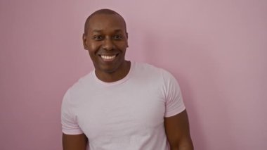 Pembe gömlekli genç adam pembe arka planda duruyor. Davetkar ve kendinden emin bir ifade sergiliyor.