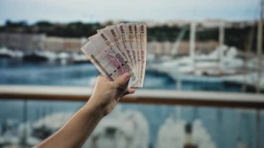 Suudi riyal banknotları tutan adam deniz kıyısında arka planda su ve botlarla görüldü..