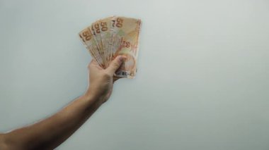 Türk lira banknotlarını beyaz bir zemin üzerinde tutan adam, döviz kuruna ve nakit akışı görüntülerine odaklanarak mali ve ekonomik temaları vurguluyor.