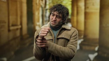 Bir sonbahar günü açık havada bileğini tutarken kederli bir ifade sergileyen kahverengi ceketli genç bir adam..