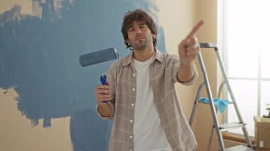 Evin arka planında mavi duvar merdiveni ve ekipman olan yeni bir evde el kol hareketi yapılmazken, tekerlekli sandalyeli bir adam ev geliştirme sahnesini işaret ediyor..