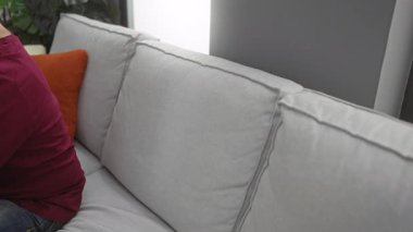 Rahat bir oturma odasında, rahat bir ortamda rahat bir ruh hali sergileyen, yumuşak yastıklarla çevrili, günlük giysiler giyen genç bir adam..