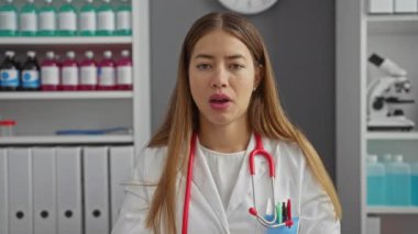 Üniformalı beyaz kadın, sessiz kalmayı savunuyor. Parmakları dudaklarında, klinik ortamda sessiz ve gizli olduğunu vurguluyor.