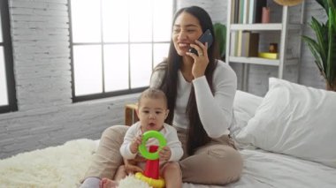 Anne, kızını yatak odasında kucağında tutarken telefonda konuşuyor. Evde sevgi ve aile sıcaklığıyla hazırlanıyor..