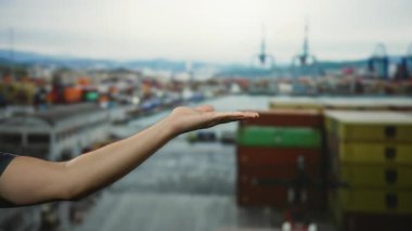 Açık liman ortamında el kol hareketi yapan bir adam, arka planda tekne ve konteynırlarla deniz kenarını işaret edip onaylıyor.