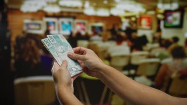 Brezilya Reais 'i elinde tutan adam, oturanların bulanık arka planıyla bir iç oda ortamında para ve iş bağlamını gösteriyor..