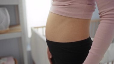 Kalbini oluşturan kadın ellerini karnına koyup yatak odasında bebek beşiğinin yanında duruyor..