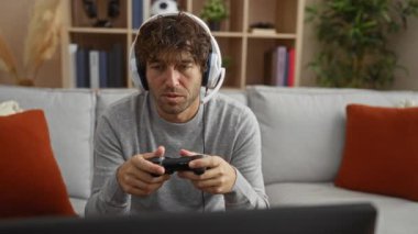 İspanyol adam evde video oyunu oynuyor kulaklık takıyor ve rahat bir oturma odasında kumanda tutuyor..