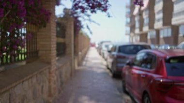 Bulanık arka planda park halindeki arabaları ve canlı çiçekleri gösteren şehir caddesi, sönmüş binalar ve renkli atmosferle sakin bir açık hava manzarası sağlıyor