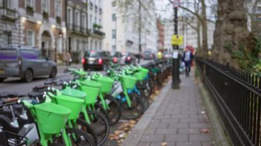 Londra 'daki bulanık cadde, bir kış günü şehir hayatını ve yeşil ulaşımı ön plana çıkaran dağılmış bisikletleri, arabaları ve yürüyen bir adamı gösteriyor..