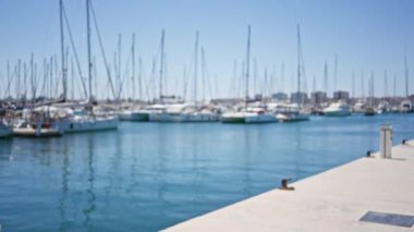 Açık mavi gökyüzü ve arka planda sakin su ile güneşli bir günde rıhtıma yanaşmış bir sürü yelkenliyle bulanık marina.