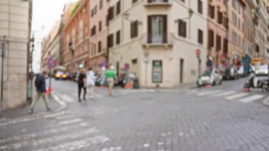Bulanık yayalar Roma, İtalya 'da bir kaldırım taşı caddesini geçiyor. Arka planda tarihi binalar ve arabalar var. Yumuşak odaklı canlı bir şehir manzarası yaratıyorlar..