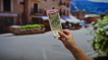 Bir şehir caddesinde elinde Hint banknotları tutan bir adamın elleri. Arka planda bulanık binalar olan bir şehir ortamında para gösteriyor..