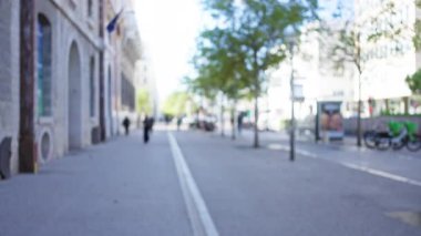 Marsilya 'daki bulanık sokak manzarası güneşli bir Avrupa şehri boyunca ağaçlar ve binalarla birlikte yürüyen bulanık insanları gösteriyor..