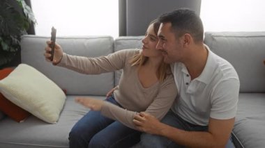 Evdeki koltukta oturan bir çift akıllı telefondan video görüşmesi yapıyor, mutlu ve samimi bir anı tasvir ediyor, doğal ışık eşliğinde rahat bir oturma odası hazırlıyorlar..