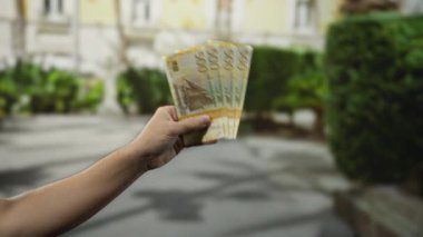 Norveç banknotlarını şehir sokaklarında arka planda tutan, şehir ortamında para ve finans gösteren, ekonomi ve seyahat yönlerini ön plana çıkaran bir adam.