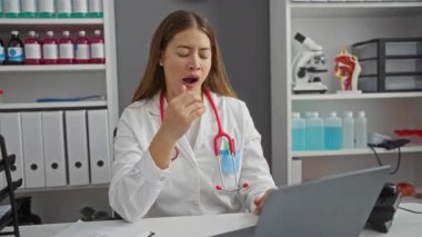 Üniformalı genç, beyaz kadın doktor. Yorgun bir ifadeyle kıt kanaat esniyor. Sıkıntıdan ve bitkinlikten dolayı klinikte uyukluyor.